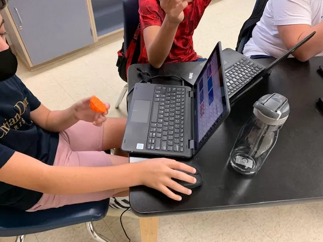 student holding 3D printed object while on a laptop