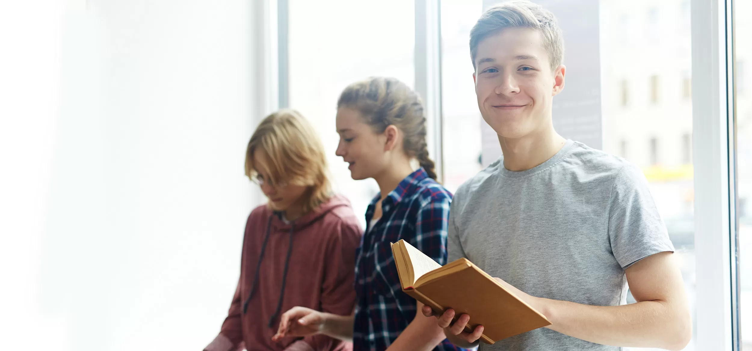 a person holding a book and smiling while two people are talking in the background