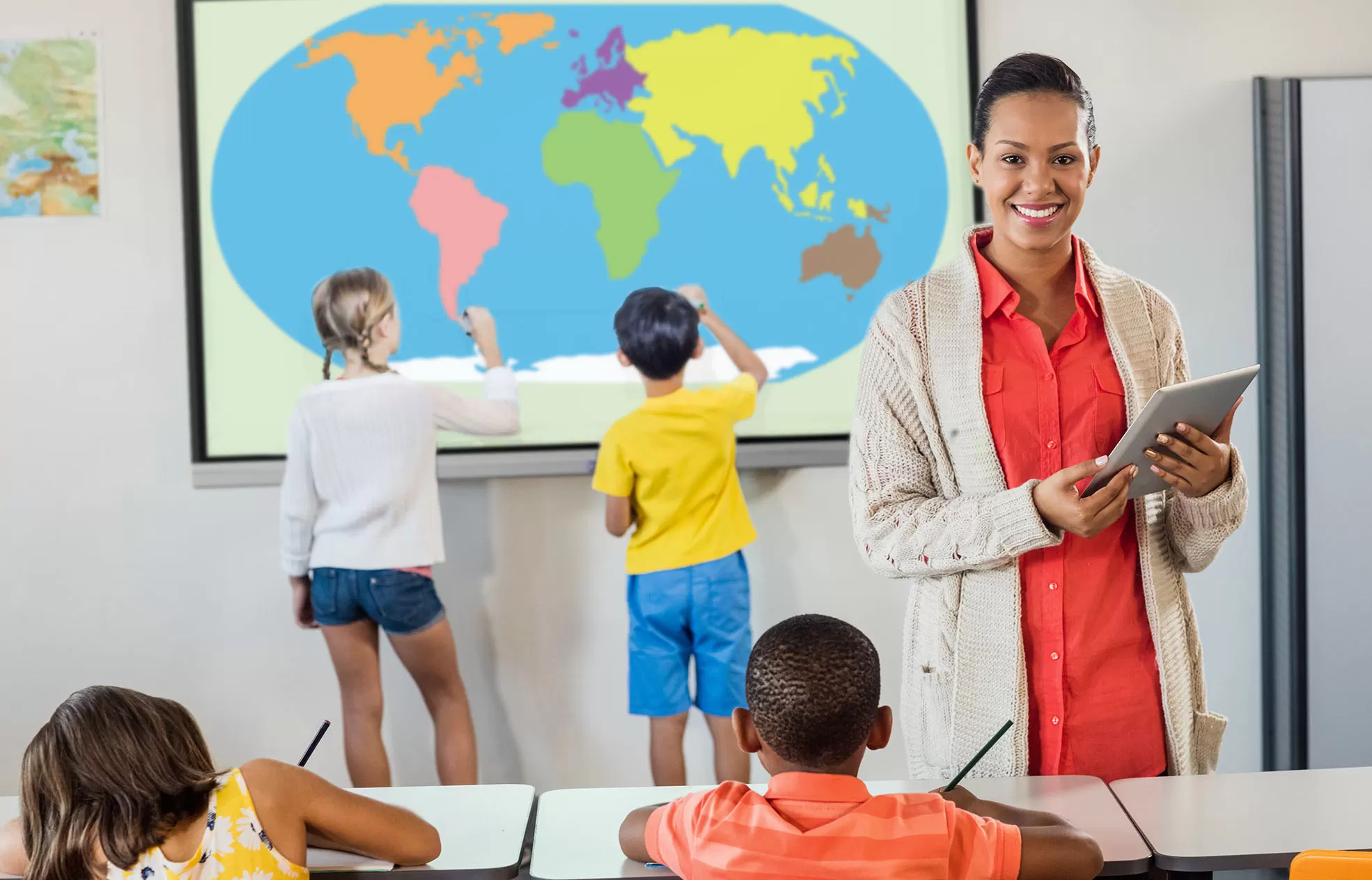 students using a Mimio-ProColor while a teacher is on a tablet facing the camera and smiling