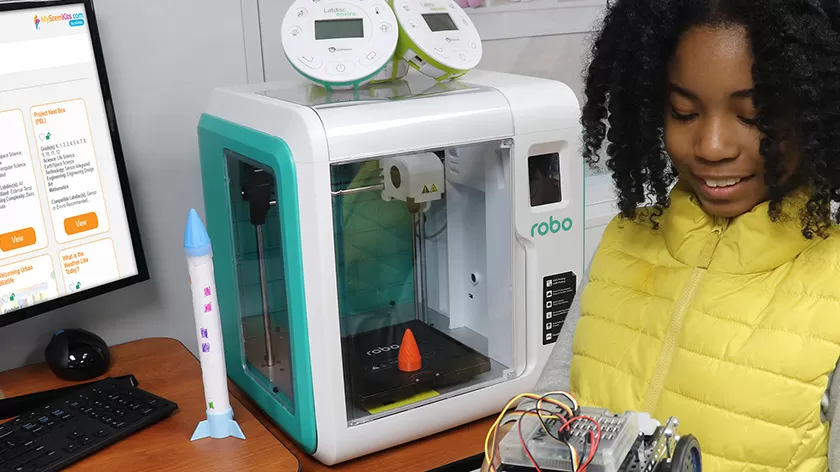 student holding a robot in front of the robo 3D printer
