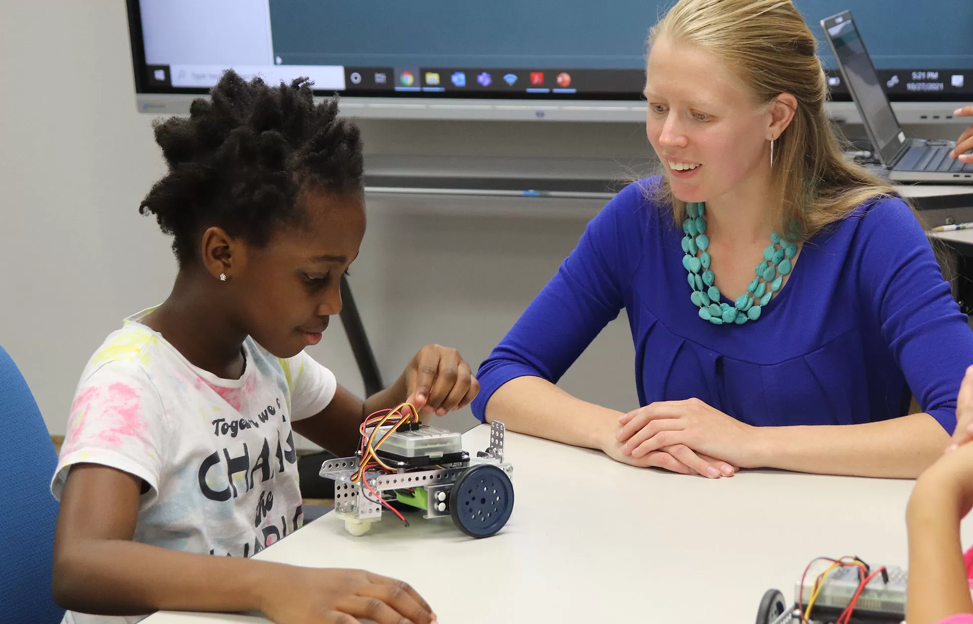 student building a wheeled robot with a teacher encouraging